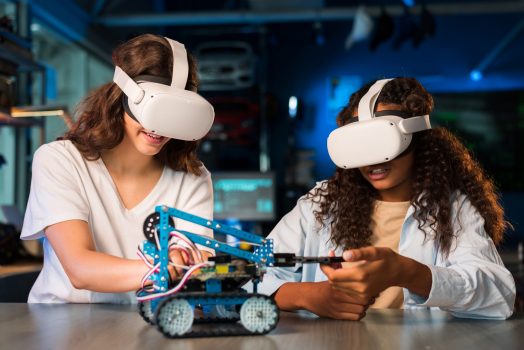 Two young women in VR glasses doing experiments in robotics in a laboratory. Robot on the table